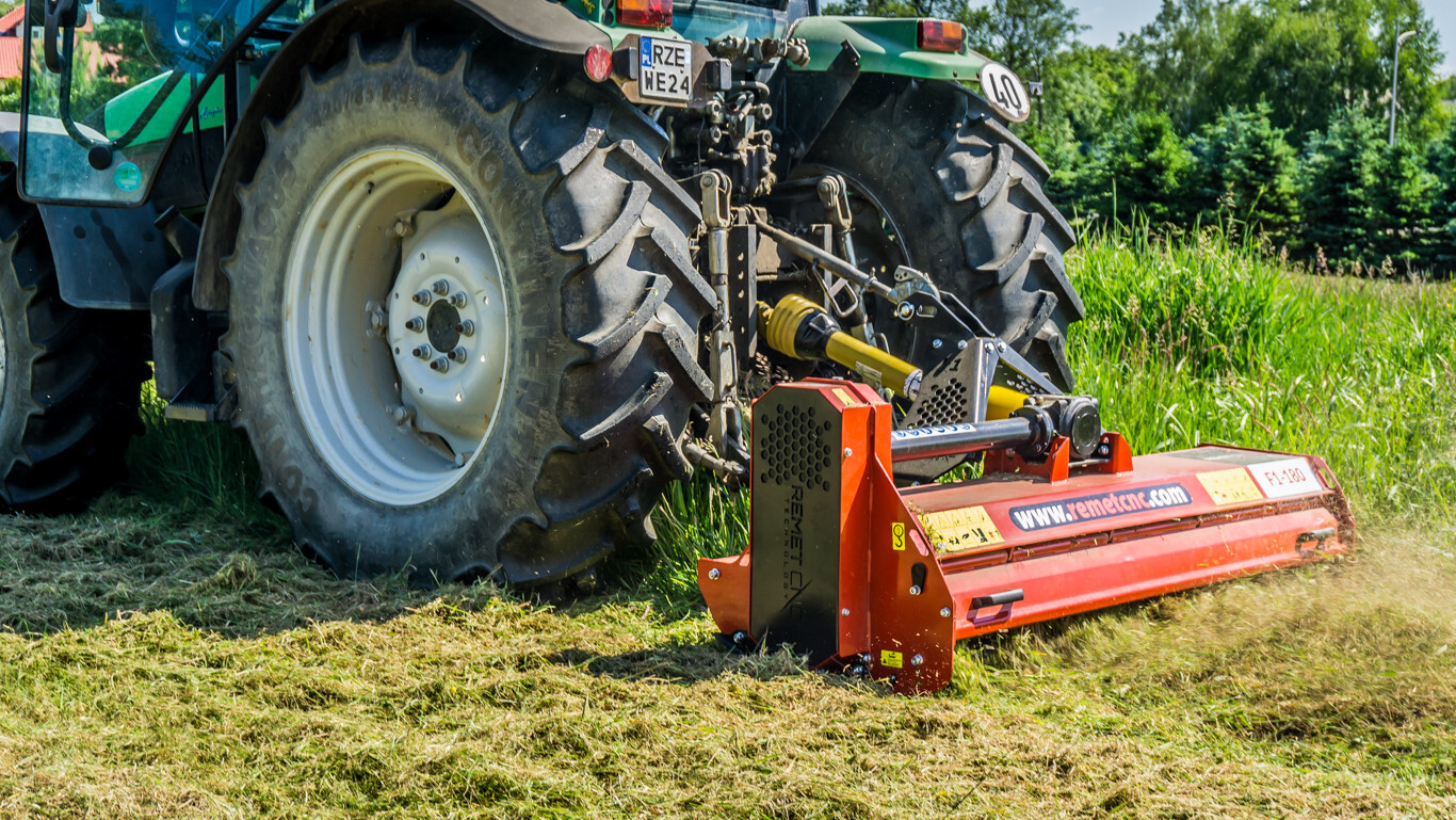 Original image of a tractor fitted with a red F1-180 flail mower cutting through long grass, showing the rear 3-point hitch and PTO shaft connection.