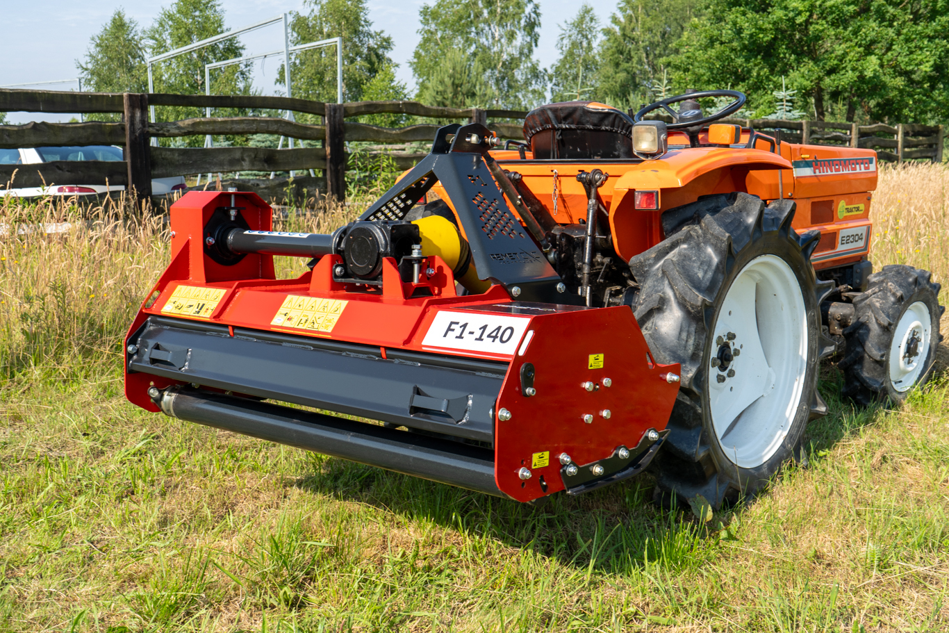  A red Remet F1-140 55" Flail Mower from Northern Woodsmen is mounted to the rear of an orange tractor, ready to cut tall grass and brush.
